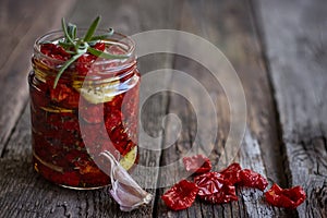 Close-up the jar of homemade sun-dried tomatoes with Provencal herbs, garlic and olive oil on a rustic wooden surface, selective