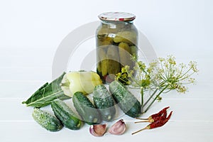 Close up of jars of canned cucumbers and fresh organic vegetables on a wooden table. A bunch of cucumbers, yellow peppers, garlic
