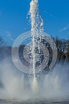 Close up of the jet of a fountain in a park with trees in the background