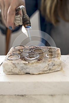 Close-up of jeweler`s hands working with a blowtorch on a piece of silver jewelry in his workshop