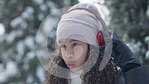 Close-up of joyful happy African American teen girl dancing and singing to music in headphones outdoors on winter day