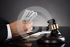 Close-up Of Judge Counting Banknote At Desk