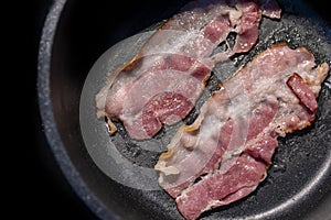 Close up juicy bacon strips frying in its own grease