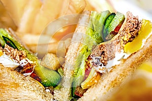 Close Up of Juicy Club Sandwich with Lectuce and Pickles with Blur French Fries in Background.