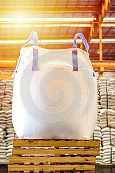 Close up of a jumbo bag on wooden pallet with background of bulk sugar bags