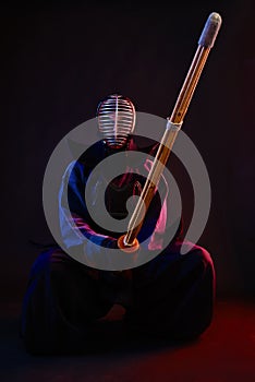 Close up. Kendo fighter wearing in an armor, traditional kimono, helmet, sitting, practicing martial art with shinai