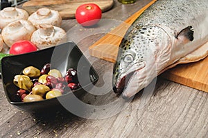 Close-up keta fish, whole on the cutting board of the kitchen table next to olives tomatoes and mushrooms. Healthy sea