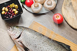 Close-up keta fish, whole on the cutting board of the kitchen table next to olives tomatoes and mushrooms. Healthy sea