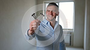 Close-up key in male hand with blurred Caucasian man smiling at background. Happy confident flat owner boasting purchase