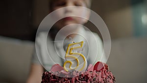 Close up of kid blowing out candle with number 5 on chocolate birthday cake in slow motion. Five years old boy