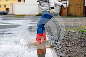 Close-up of kid boy wearing red rain boots and walking during sleet and rain on rainy cloudy day. Child in colorful