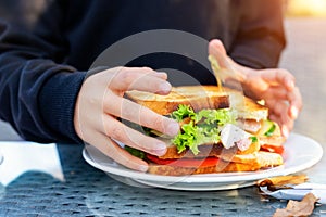 Close-up kid girl hand eating hamburger with ham and fresh vegeatables at cafe on bright sunny day outdoors. Fast food children