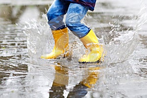 Close-up of kid wearing yellow rain boots and walking during sleet, rain and snow on cold day