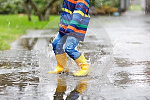 Close-up of kid wearing yellow rain boots and walking during sleet, rain and snow on cold day. Child in colorful fashion