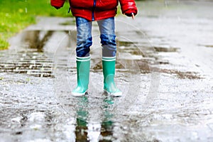 Close-up of kid wearing yellow rain boots and walking during sleet, rain and snow on cold day. Child in colorful fashion