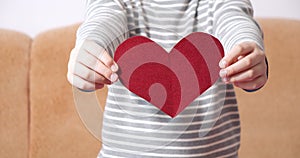 Close-up of kids hands holding a red heart-shaped postcard and showing her to the camera. Valentine`s day concept