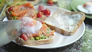 Close up of knife cutting toast with pouched egg, avocado and salmon. slow motion