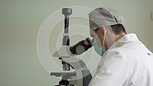 Close-up of a laboratory assistant in a medical uniform examines a biomaterial taken through a microscope. Laboratory medical rese