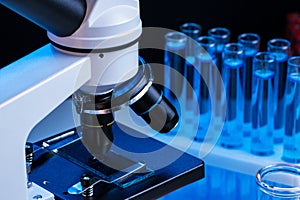 Close up of laboratory microscope with set of test tubes with blue liquid