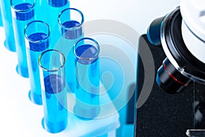 Close up of laboratory microscope with set of test tubes with blue liquid