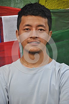 Close up of a Ladakhi young guy looking at camera, standing against Buddhist prayer flags