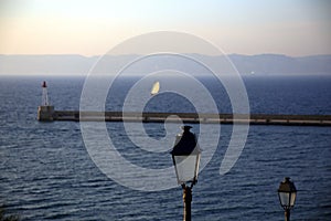 Close up of a lamppost, near the sea, with the background of the pier and a sailing boat, Parc National des Calanques, Marseille,