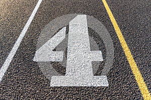 Close up lane number four, 4, on a new black running track with white lane lines and other markings.