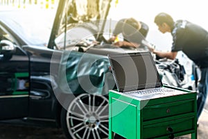Close up laptop or computer notebook interfaced with car for repair during two repairman work investigate problem program and