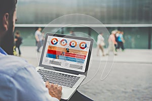 Close-up laptop with graphs, diagrams and charts on screen in hands of businessman sitting outdoors and working.