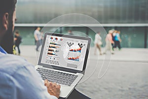 Close-up laptop with graphs, diagrams and charts on screen in hands of businessman sitting outdoors and working.