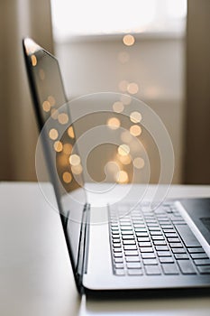 Close up of laptop keyboard with blank screen on a table by blurry bokeh lights background in the house or office modern