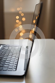 Close up of laptop keyboard with blank screen on a table by blurry bokeh lights background in the house or office modern