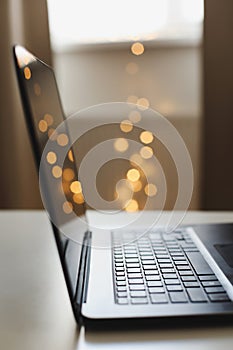 Close up of laptop keyboard with blank screen on a table by blurry bokeh lights background in the house or office modern