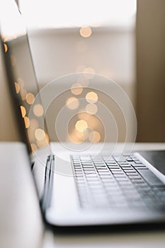 Close up of laptop keyboard with blank screen on a table by blurry bokeh lights background in the house or office modern