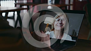 A close-up on a laptop screen with a smiling adult woman waving at the camera.