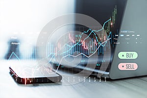 Close up of laptop and smartphone on desk creative candlestick trading graph on blurry background.