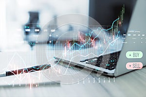 Close up of laptop and supplies on desk creative candlestick trading graph on blurry background. Selling and buying stocks, market