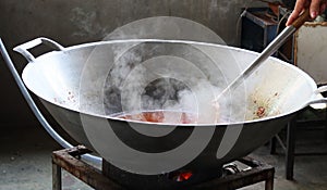 Close-up, large iron pan cooking, smoke and heat inside the kitchen.