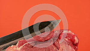 Close-up of a large kitchen knife cuts a fresh raw piece of meat on a bright orange background. Cutting pork meat. Cooking fresh m