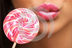 Close-up of a large pink striped Lollipop and a girl`s lips in a kiss. Beautiful pink lipstick, cosmetics