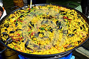 Close up of large portion of traditional Spanish paella dish freshly being cooked with seafood and rice in a frying pan at a stree