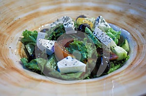 Close-up of a large round white-brown dish with Greek salad with cheese, vegetables, lettuce