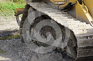 Close-up of a large track-type tractor excavator with muddy wheels on a sunny day