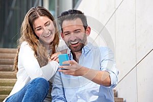 Close up laughing couple sitting on steps together with mobile phone