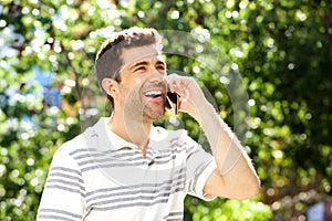 Close up laughing young guy standing outdoors and talking on mobile phone