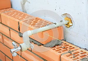 A close-up on laying face clay bricks to a concrete block wall with an outside water spigot, garden faucet