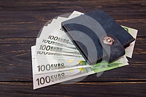 Close-up of a leather man`s wallet and one hundred euro banknotes on a wooden background