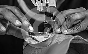 Close up of Leather sewing machine in action in a workshop with hands working in black and white