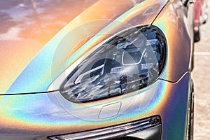 Close-up LED headlight expensive car part with exclusive iridescent painting. Vehicle covered with vibrant chameleon