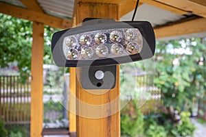 Close-up of an LED spotlight, a spotlight on a wooden post of an open veranda, on a blurred background of the garden. A